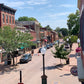 Small town street with brick buildings, parked cars, and trees on a sunny day.