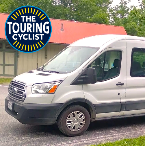 White van parked in front of a building with 'The Touring Cyclist' logo.
